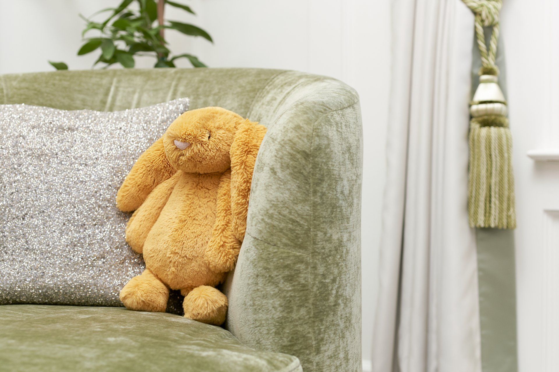 A stuffed bunny is sitting on a green couch next to a pillow.