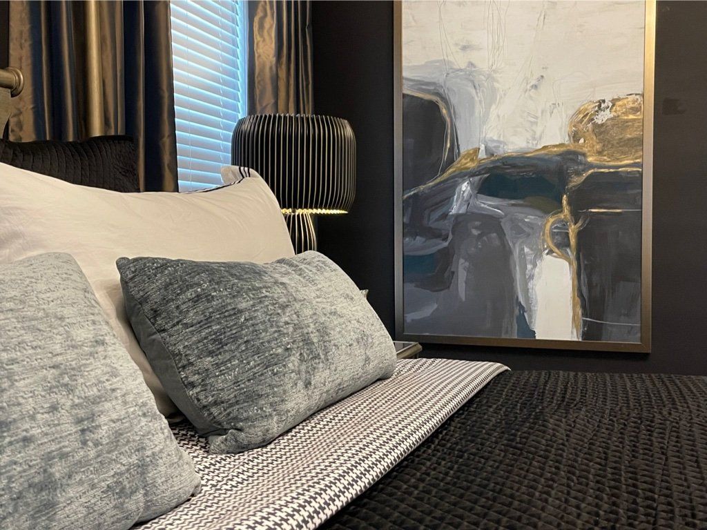 A bedroom with a bed , pillows , a lamp and a painting on the wall.