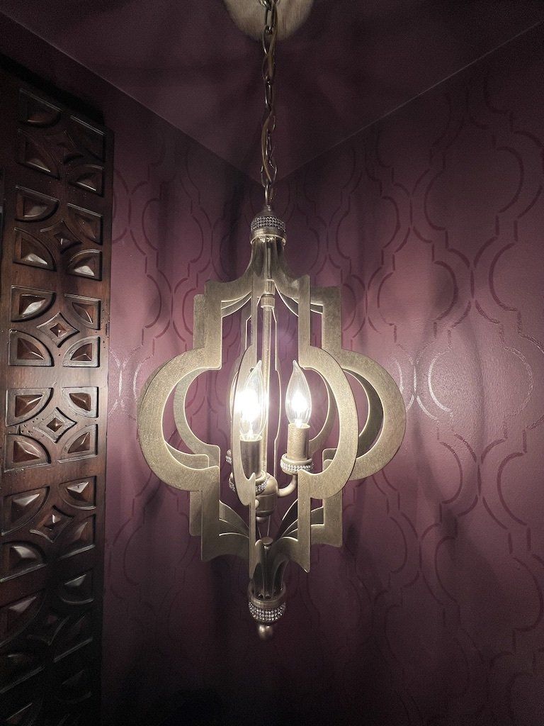 A chandelier is hanging from the ceiling in front of a purple wall.