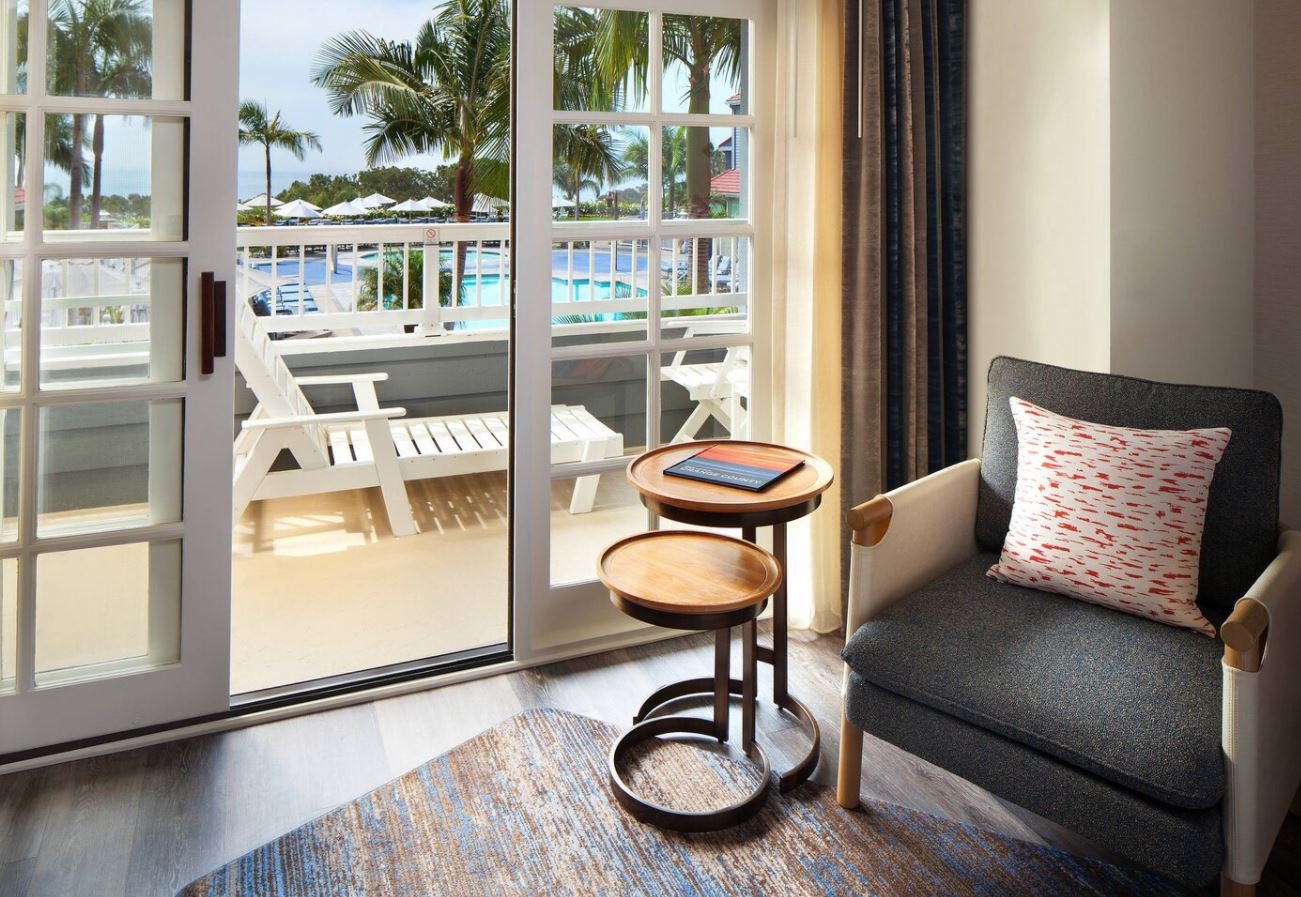 A hotel room with a chair , table and sliding glass doors leading to a balcony.