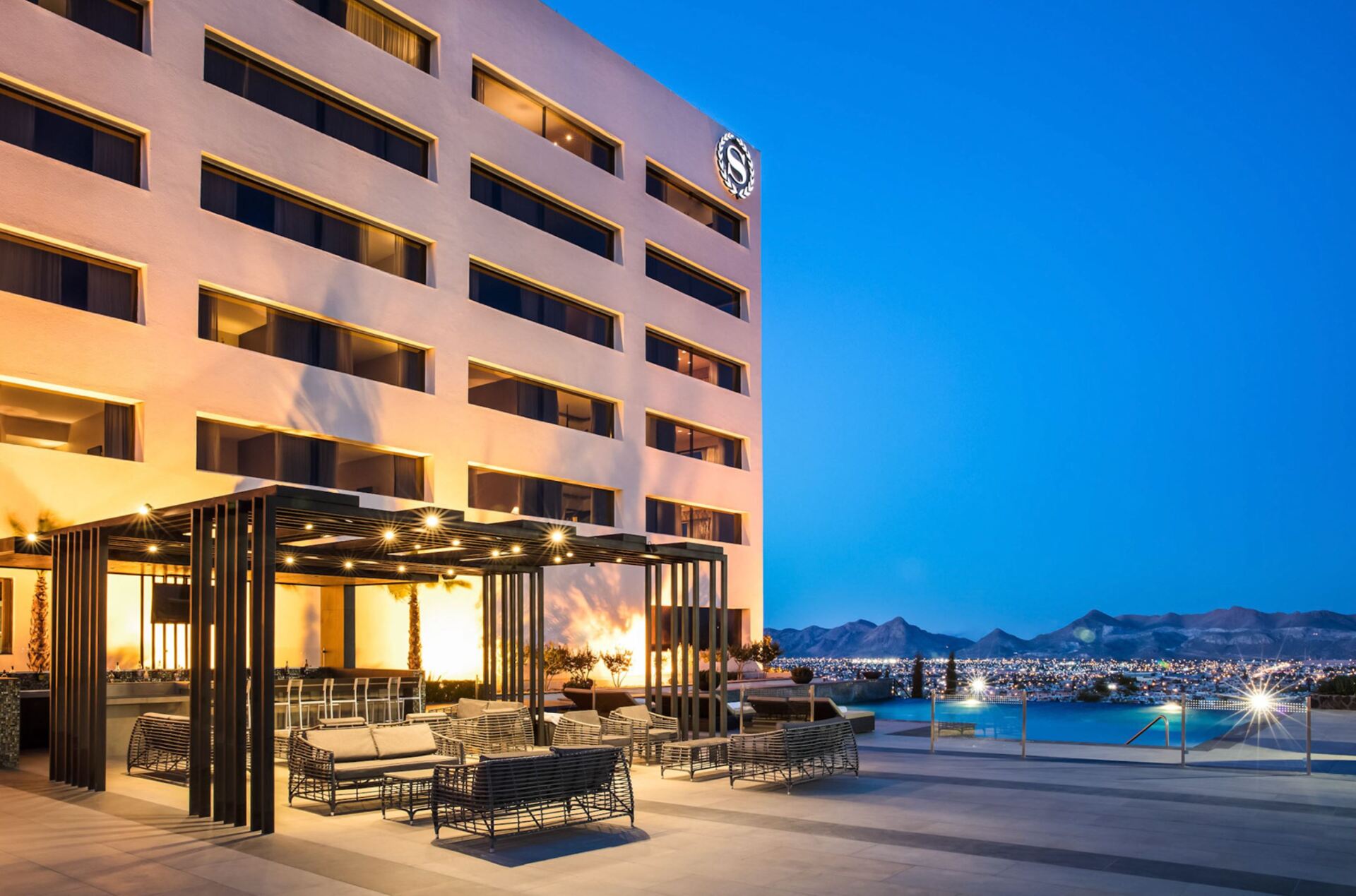 A large building with a swimming pool in front of it at night.