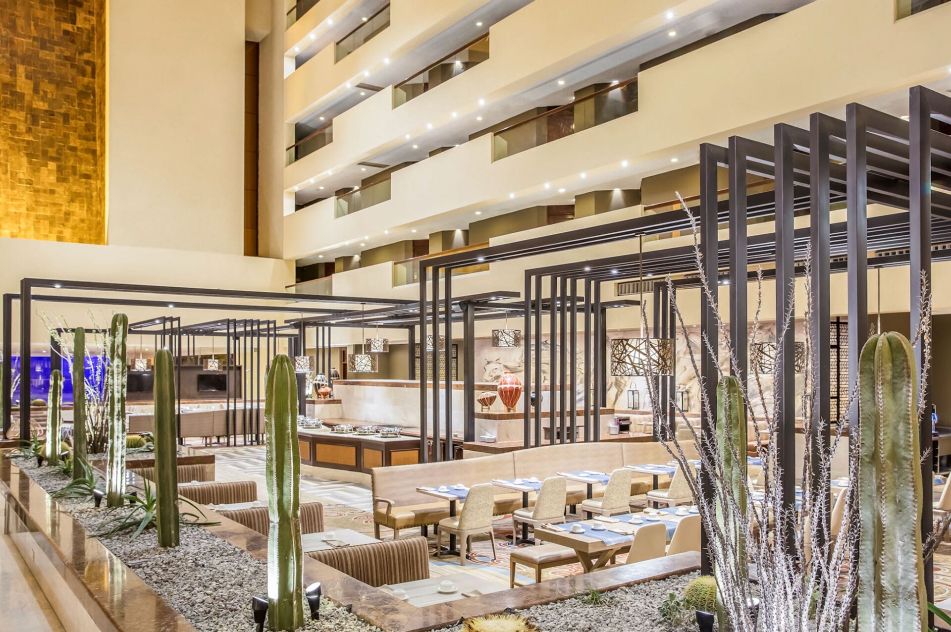 A large lobby of a hotel with tables and chairs and cactus.