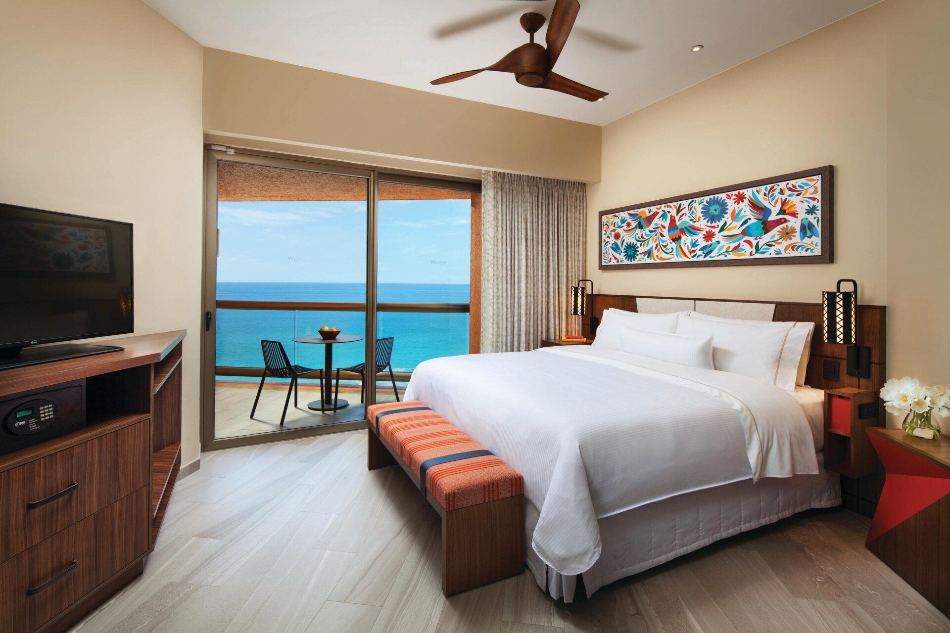 A hotel room with a king size bed , television , and balcony overlooking the ocean.