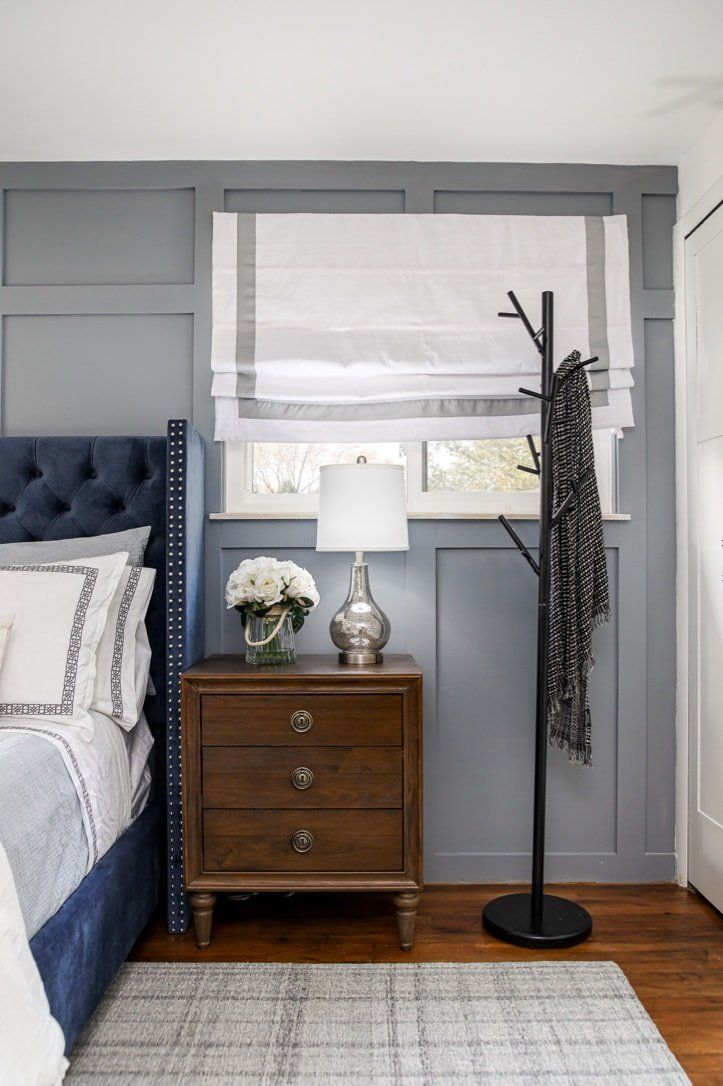 A bedroom with a bed , nightstand , lamp and coat rack.