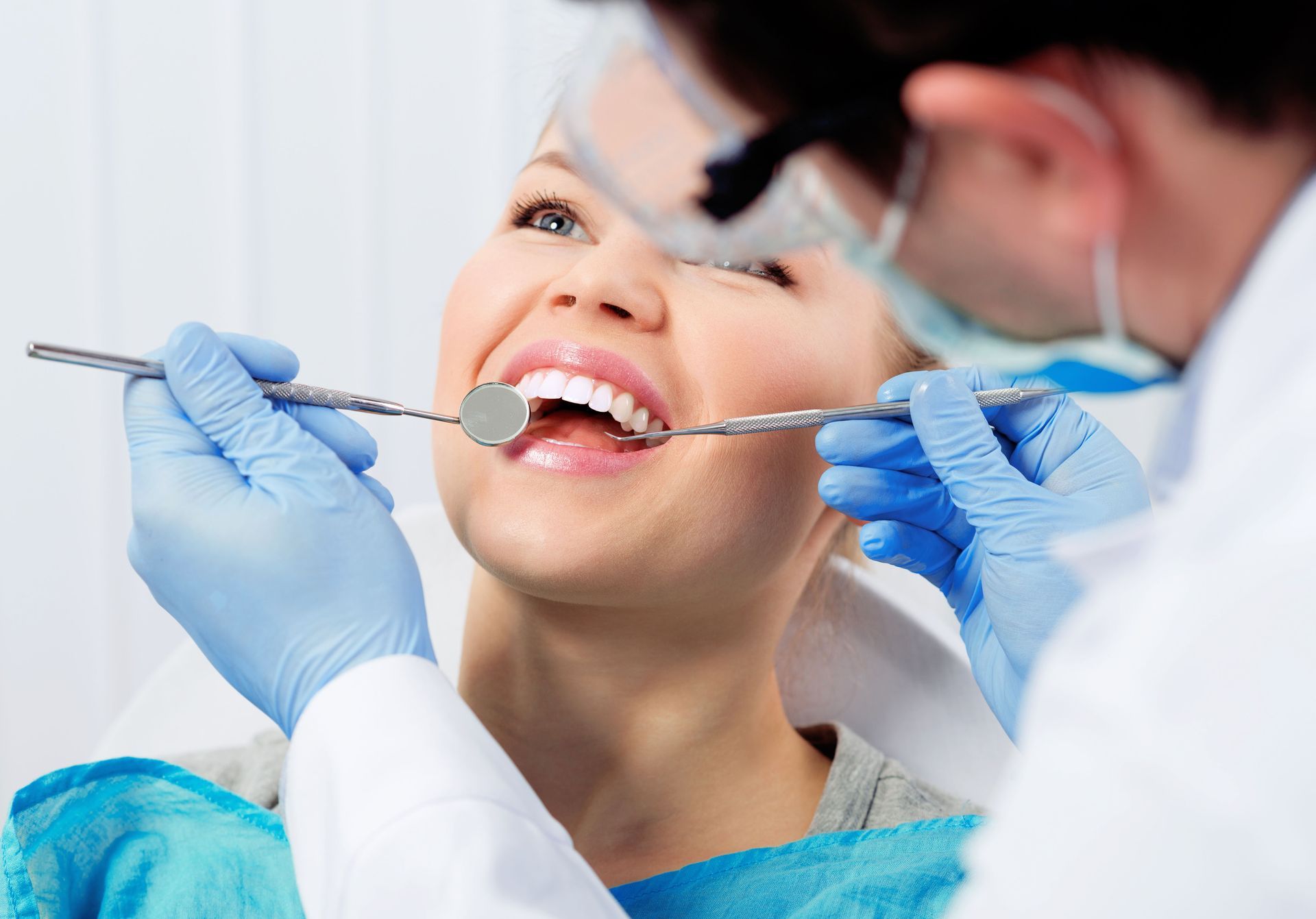 Dentist examining a woman's teeth with a mirror and probe. The woman smiles while in the dentist chair.
