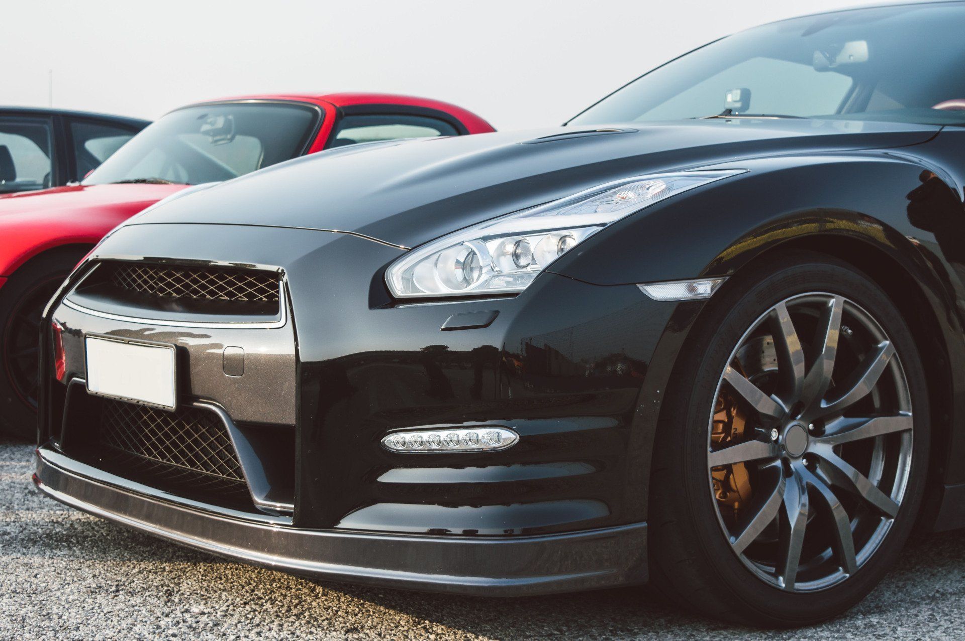 Black Nissan GT-R sports car with silver rims, parked next to a red car.