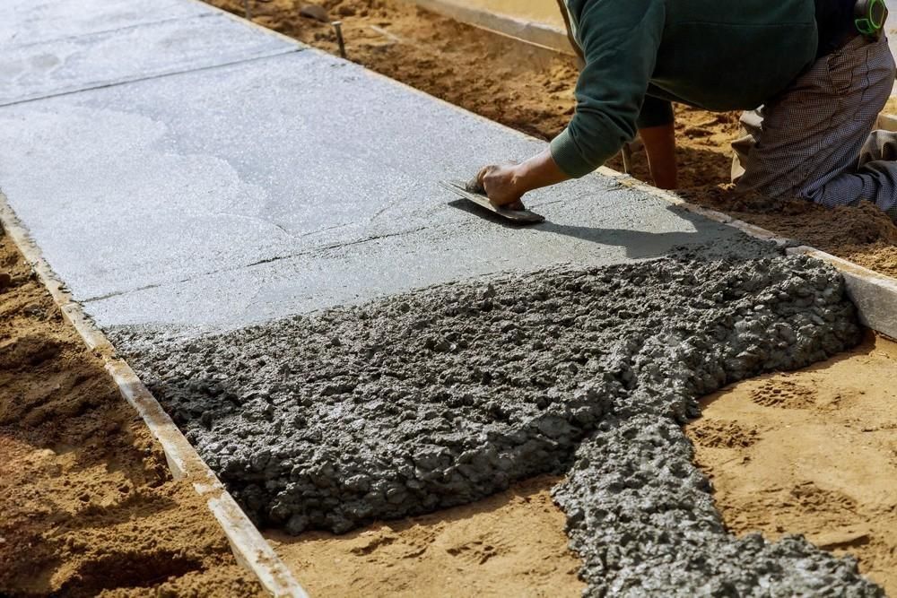 A man is spreading concrete on a sidewalk.