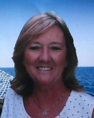 A woman in a white polka dot shirt is smiling in front of the ocean