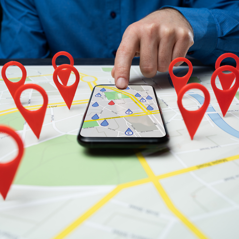 A person is using a cell phone on a map with red markers.