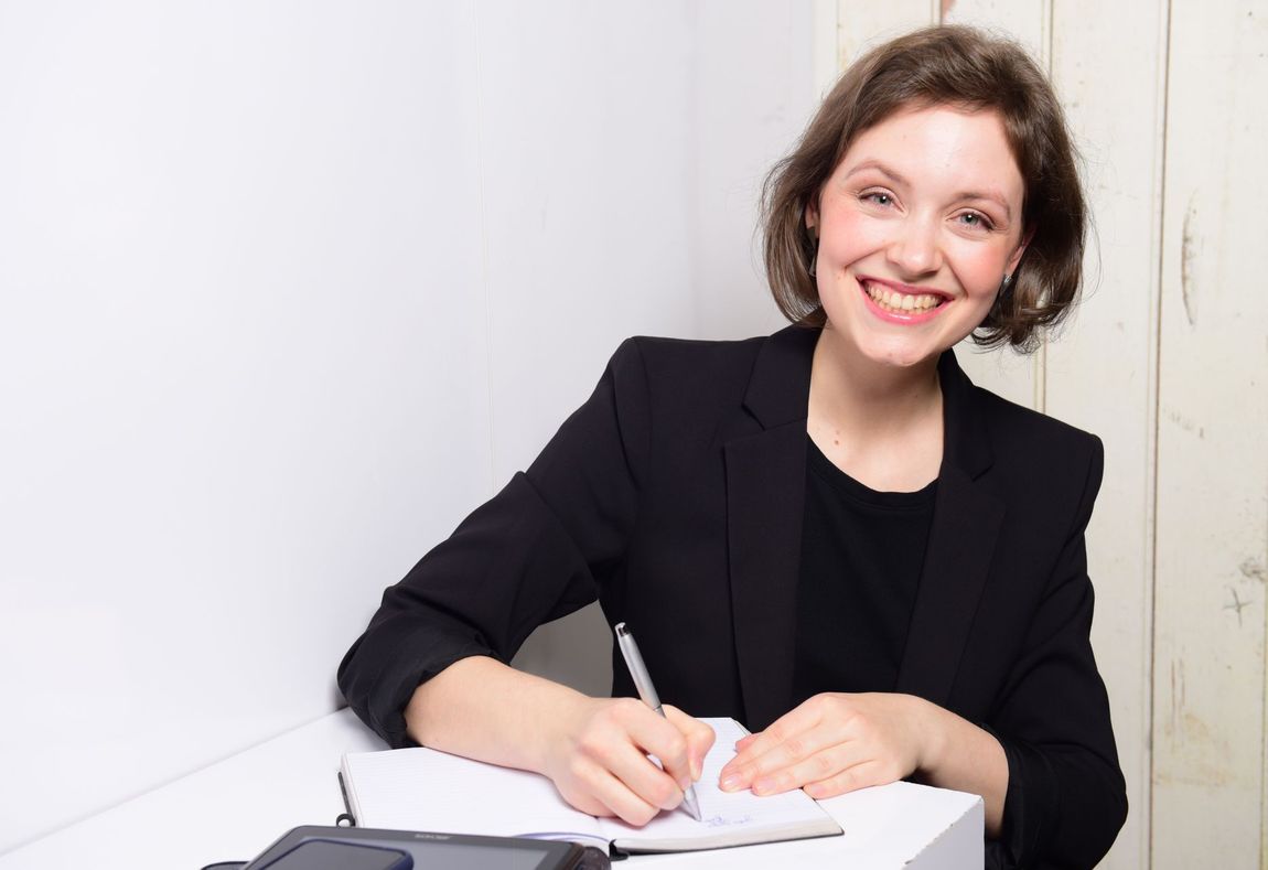 Frau sitzt an Tisch und schreib in ein Notizbuch.