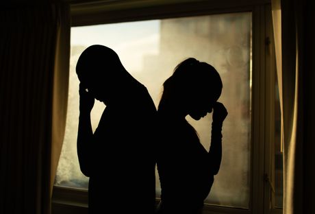 A man and a woman are standing back to back in front of a window.