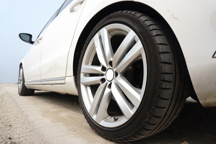 Close-up of a white car’s front wheel and tyre parked on a sandy road