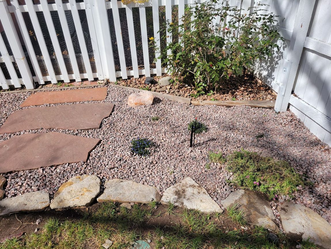 A white picket fence is surrounded by rocks and gravel in a yard.