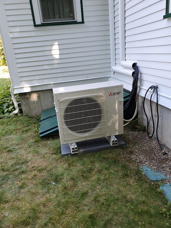 A white air conditioner is mounted on the side of a house.