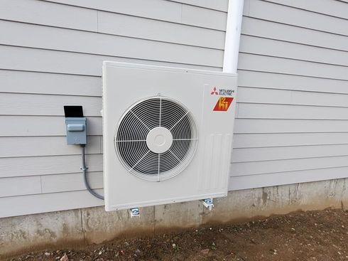 A white air conditioner is mounted on the side of a house.