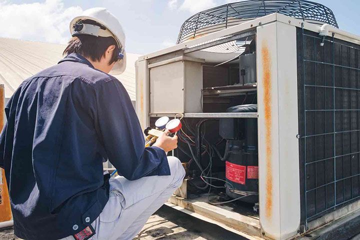 A man is working on an air conditioner on a roof.