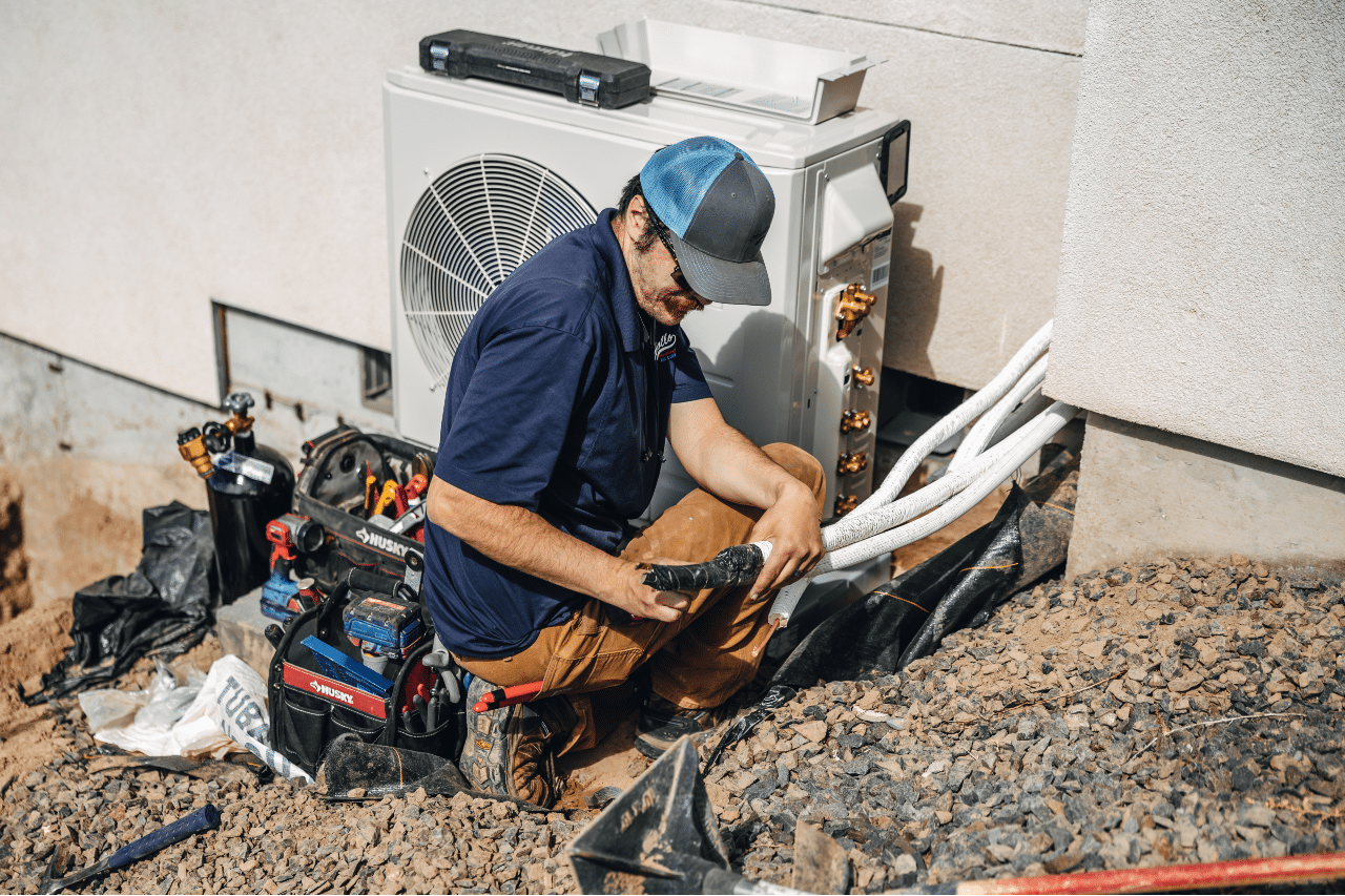 A man is sitting on the ground working on an air conditioner.
