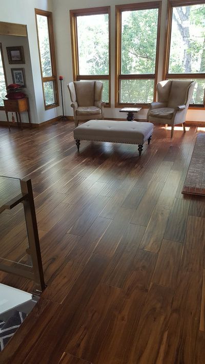 A living room with hardwood floors , chairs , ottoman and lots of windows.