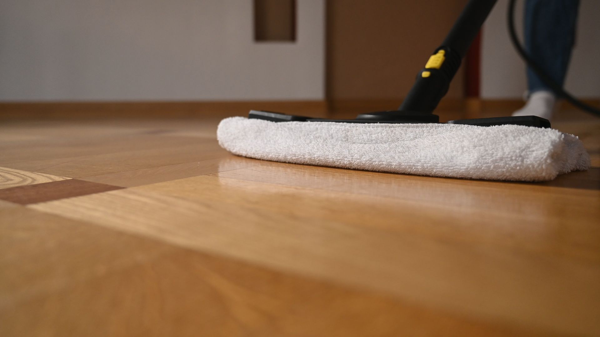 A person is using a steam mop to clean a wooden floor.