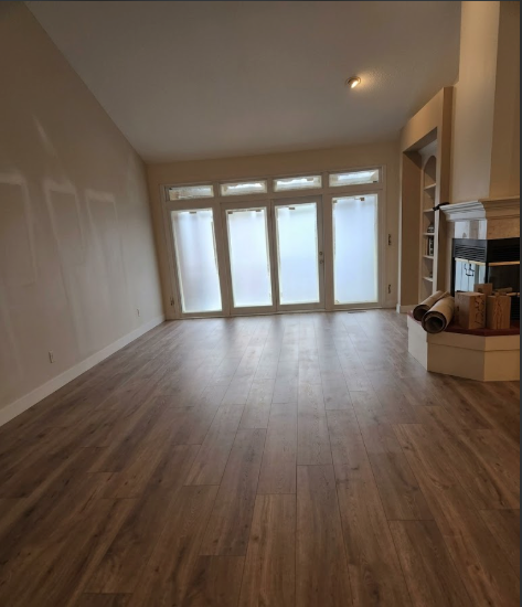 Empty living room with wood floors, sloped ceiling, and large glass doors leading outside.