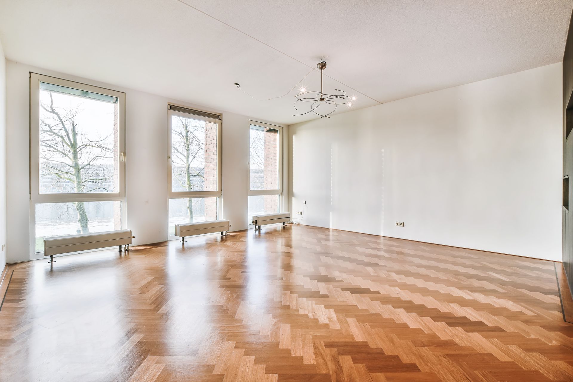 An empty living room with a wooden floor and white walls.