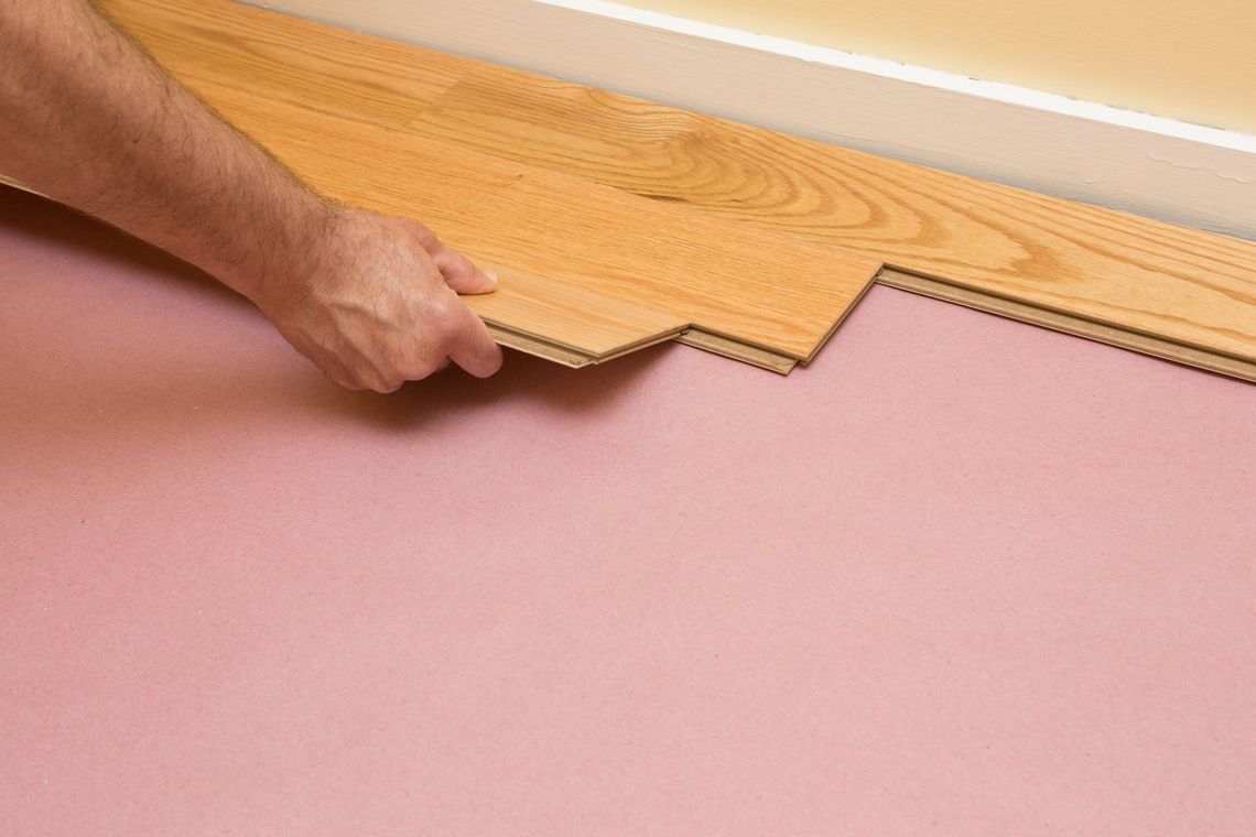 A person is laying a wooden floor on the floor.