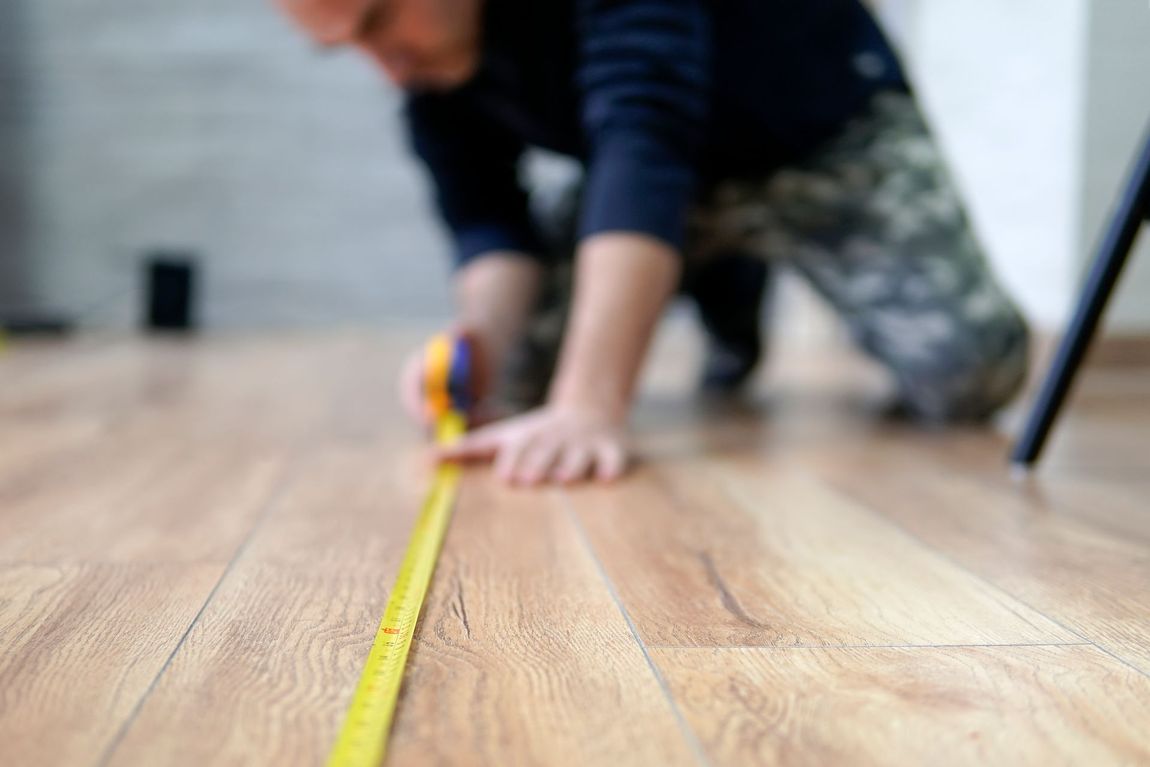 A man is measuring a wooden floor with a tape measure.