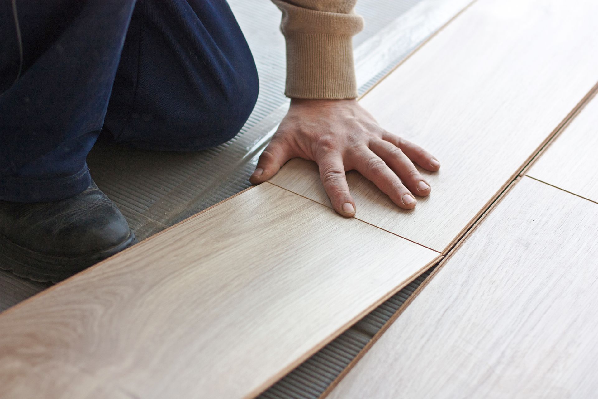 Person installing light wood flooring, aligning a plank over underlayment