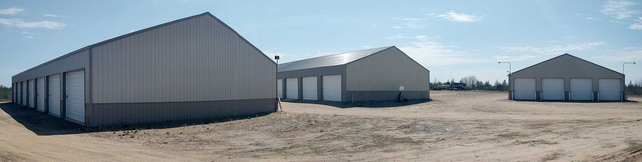 Three gray metal storage buildings against a blue sky. Buildings are in a brown dirt parking lot.