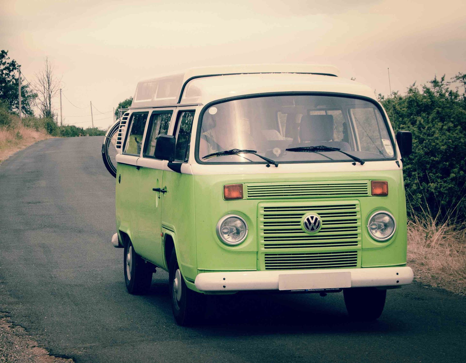Green and white vintage Volkswagen bus driving on a rural road.