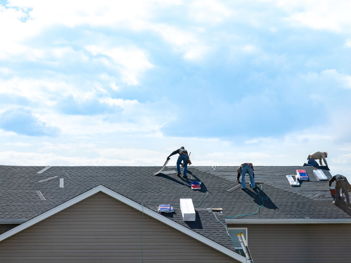 Roofers installing shingles on a house roof under a cloudy sky
