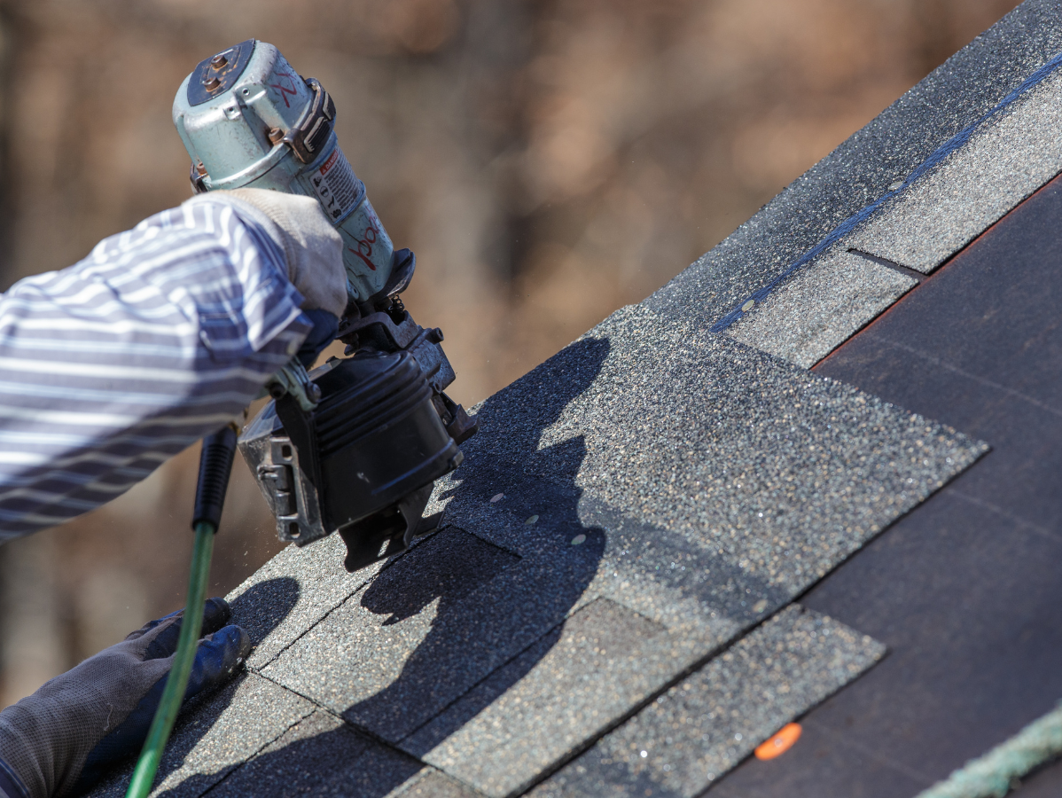 Roofing worker applying shingles with a nail gun on a sloped roof