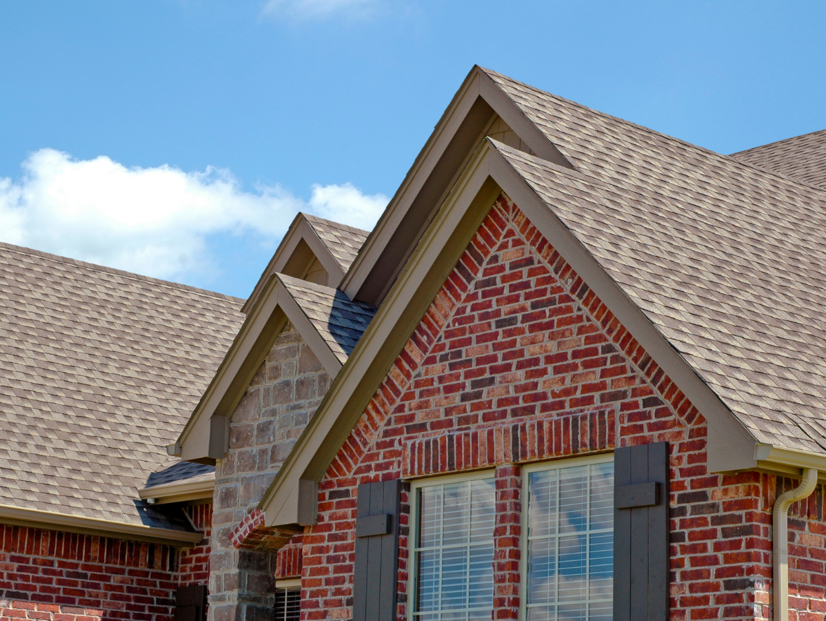 Brick house roof with gables, blue shutters, and a partly cloudy sky