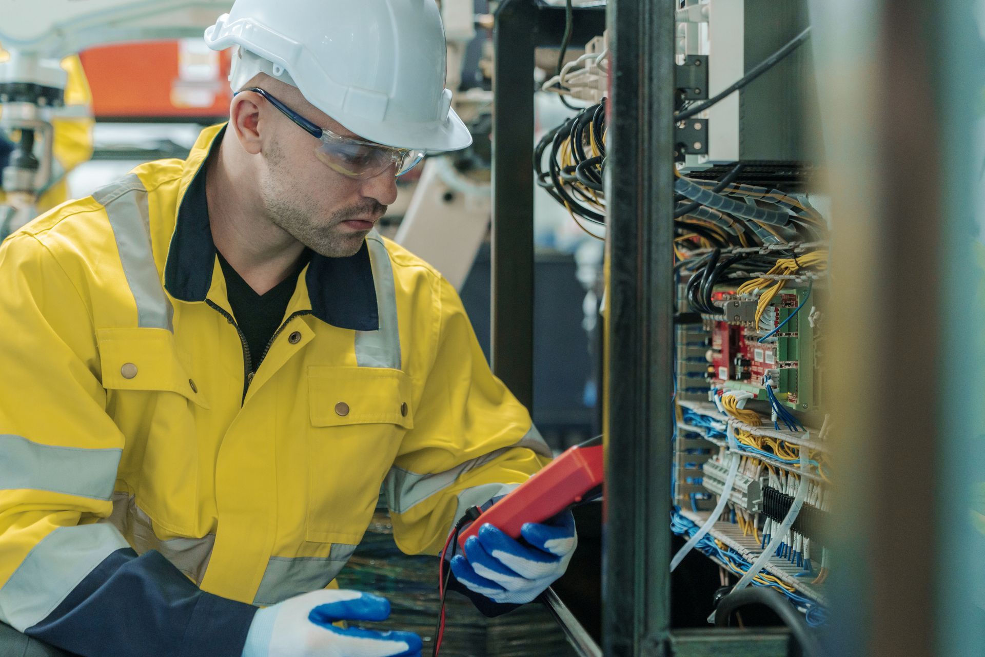 Electrician in a yellow uniform uses a multimeter on an electrical panel.