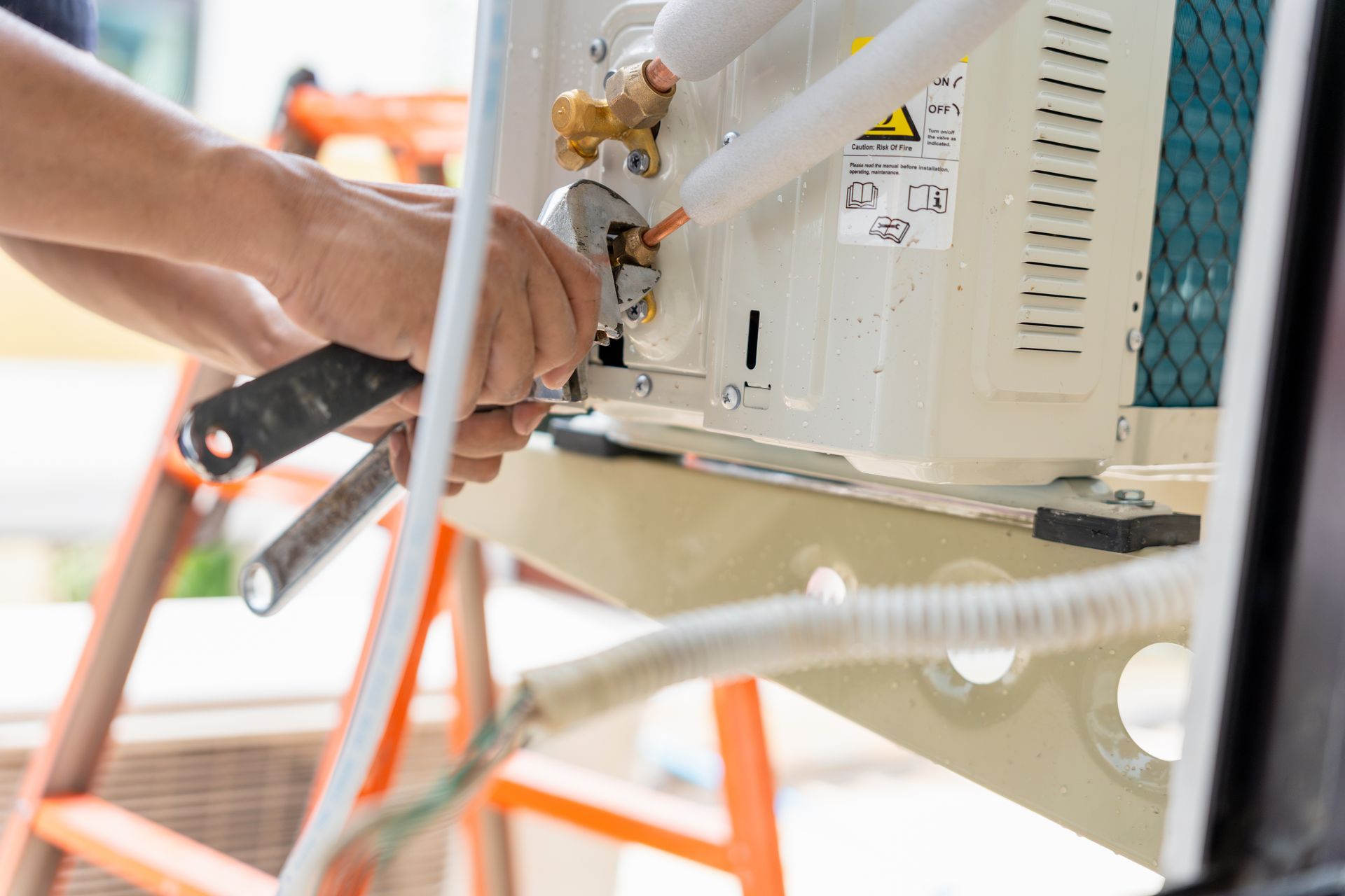 Person using a wrench to repair an air conditioning unit; outdoors.
