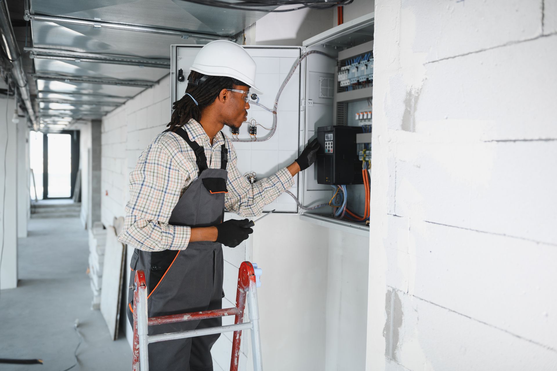Electrician working on electrical panel in a construction site, wearing a hard hat and gloves.