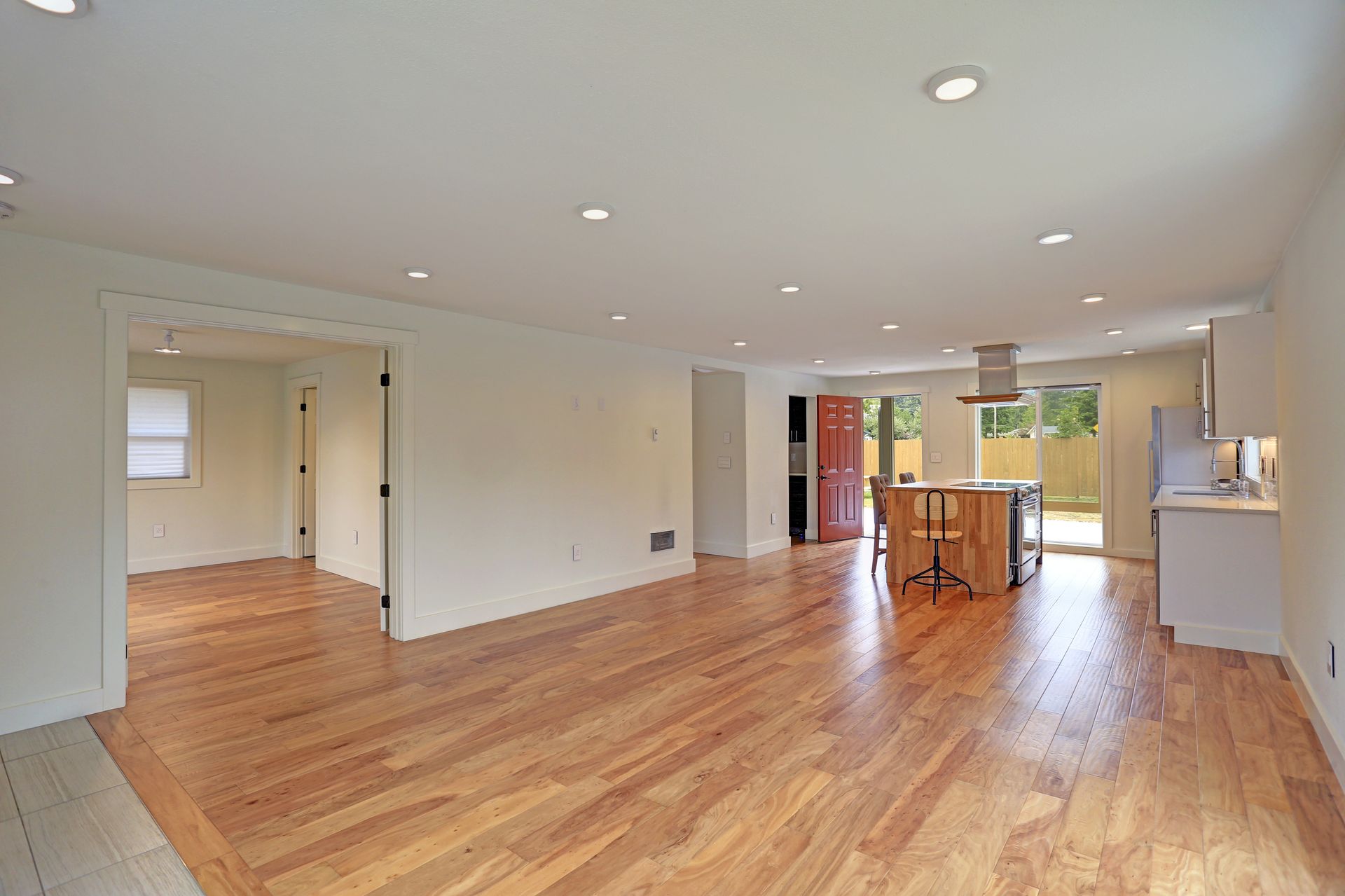 Empty open-concept living space with hardwood floors, recessed lighting, and a kitchen island.