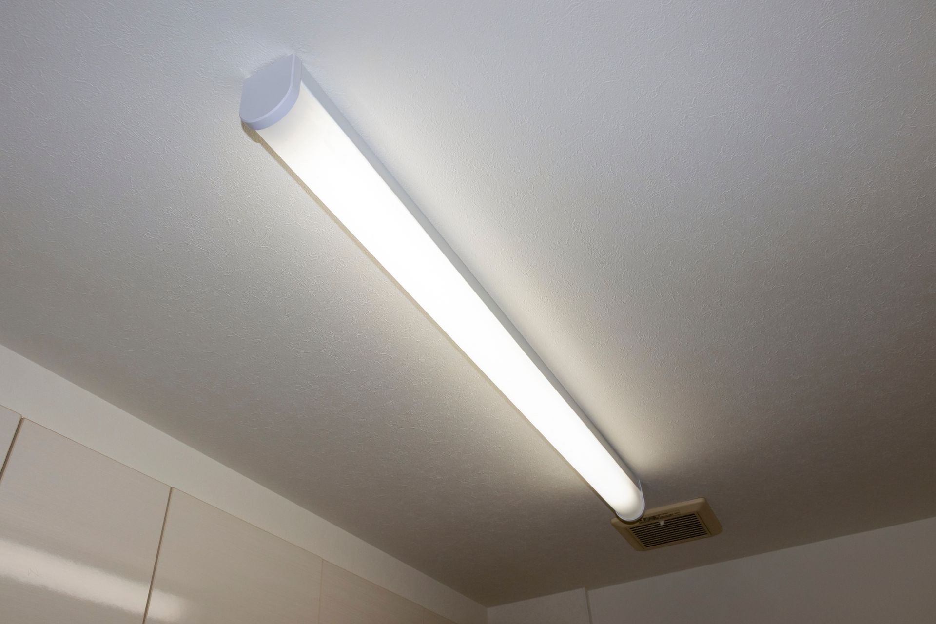 A long, white fluorescent light fixture mounted on a white ceiling.