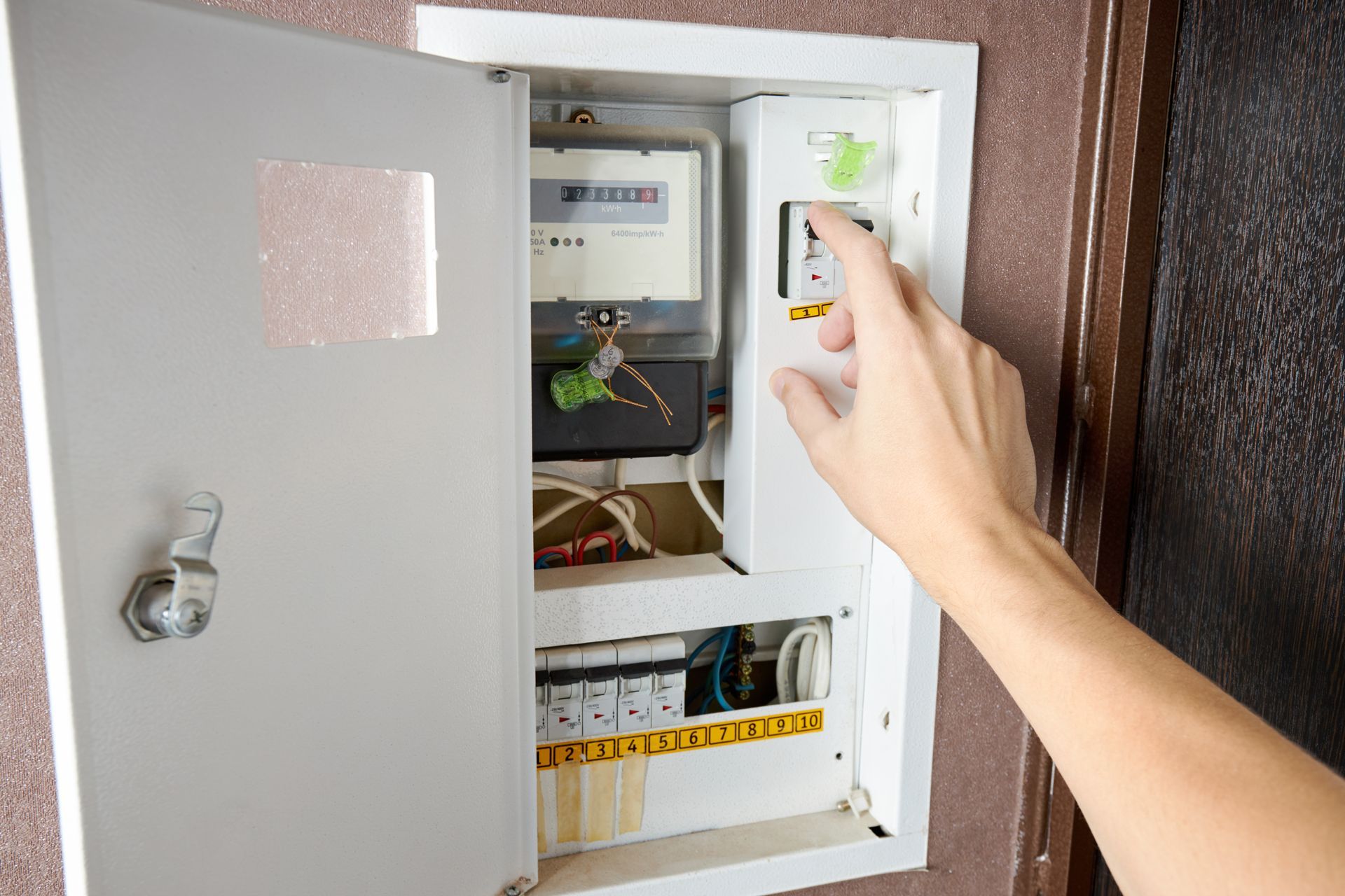 Hand reaching to turn on a circuit breaker inside an open electrical panel.