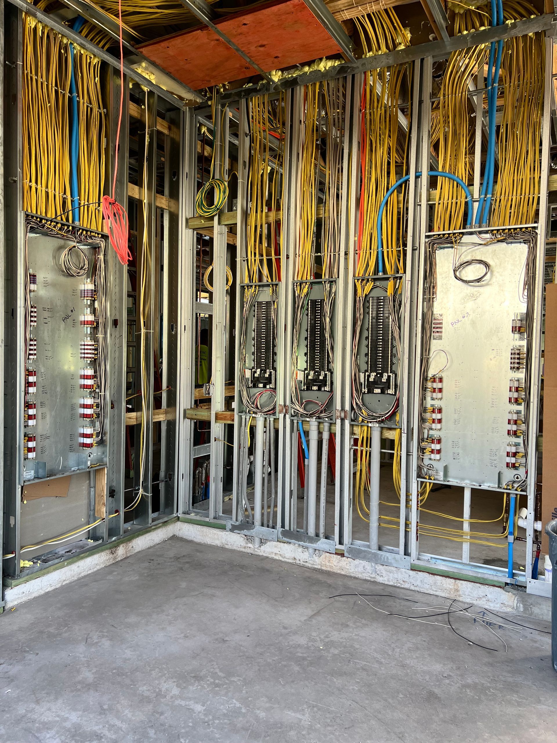 Electrician in a yellow uniform uses a multimeter on an electrical panel.