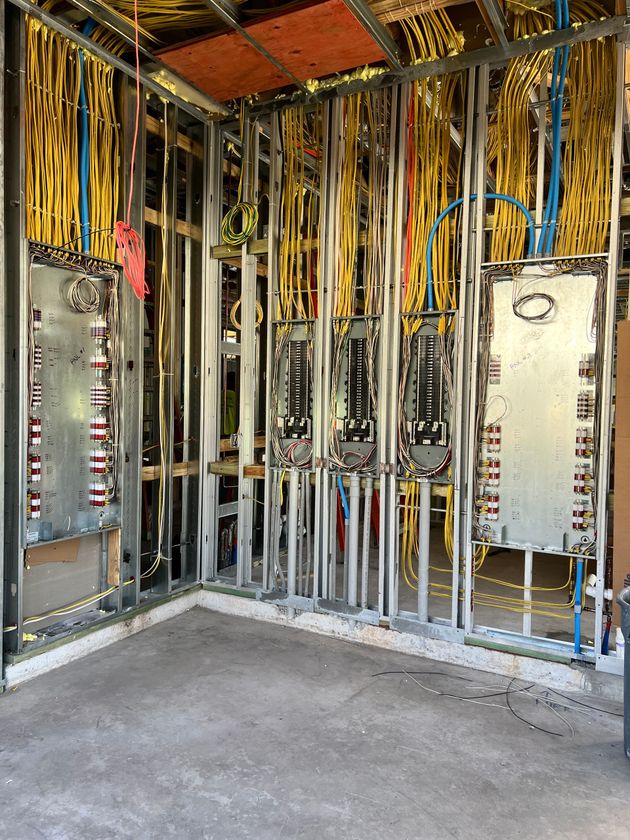 Electrician in a yellow uniform uses a multimeter on an electrical panel.