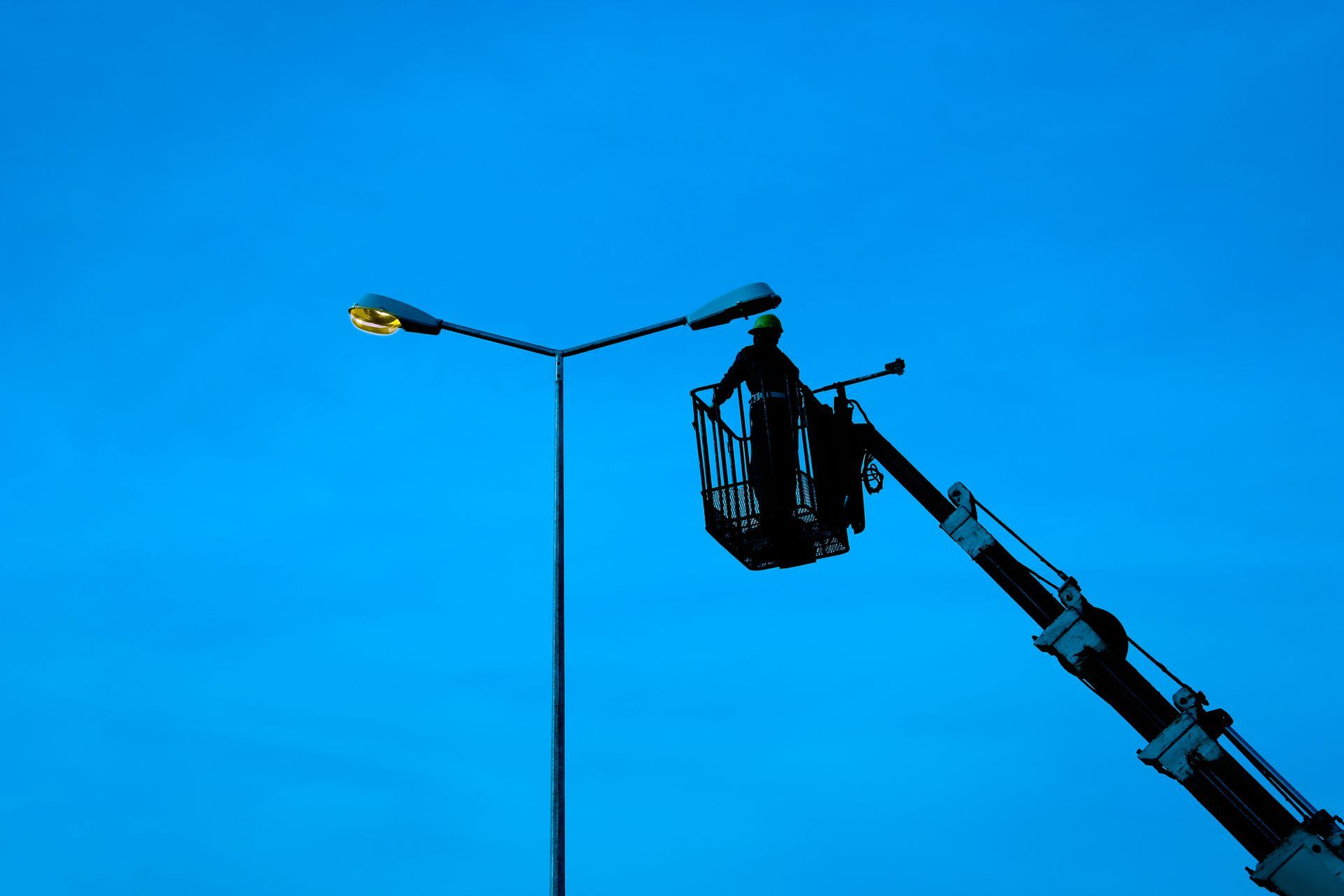 Person in a lift basket repairing a street light against a blue sky.