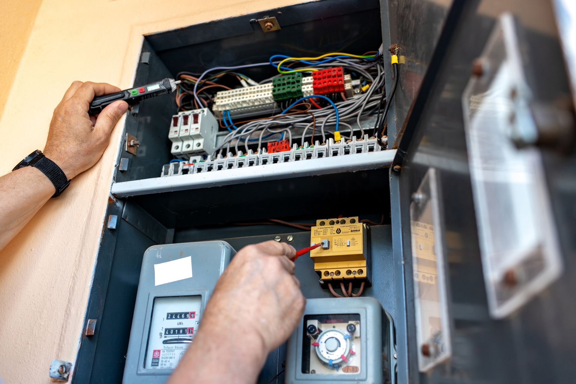 Electrician working on electrical panel, using a tool to check wires.