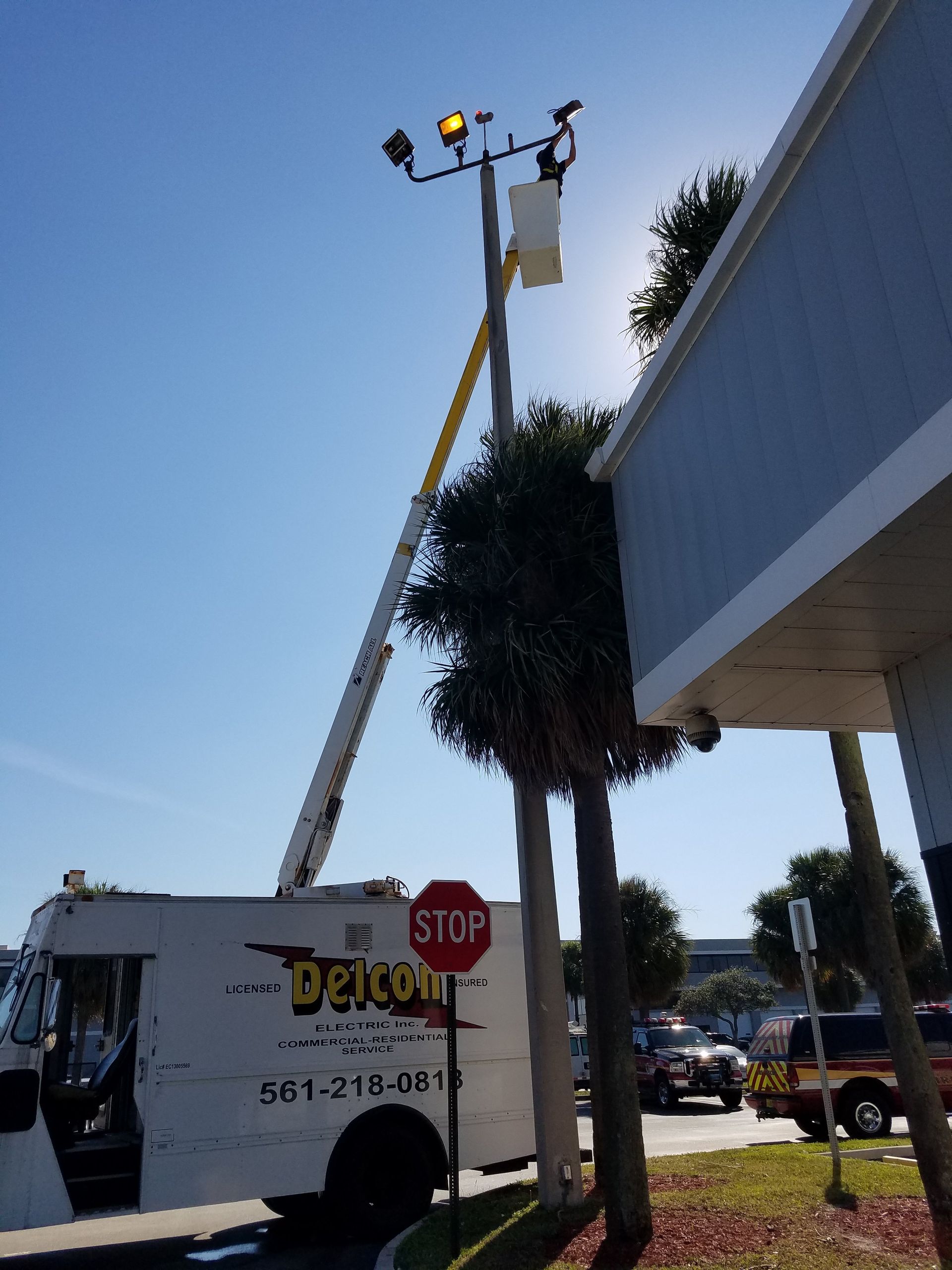 A bucket truck with a raised boom working on a light pole near a building under a sunny sky.