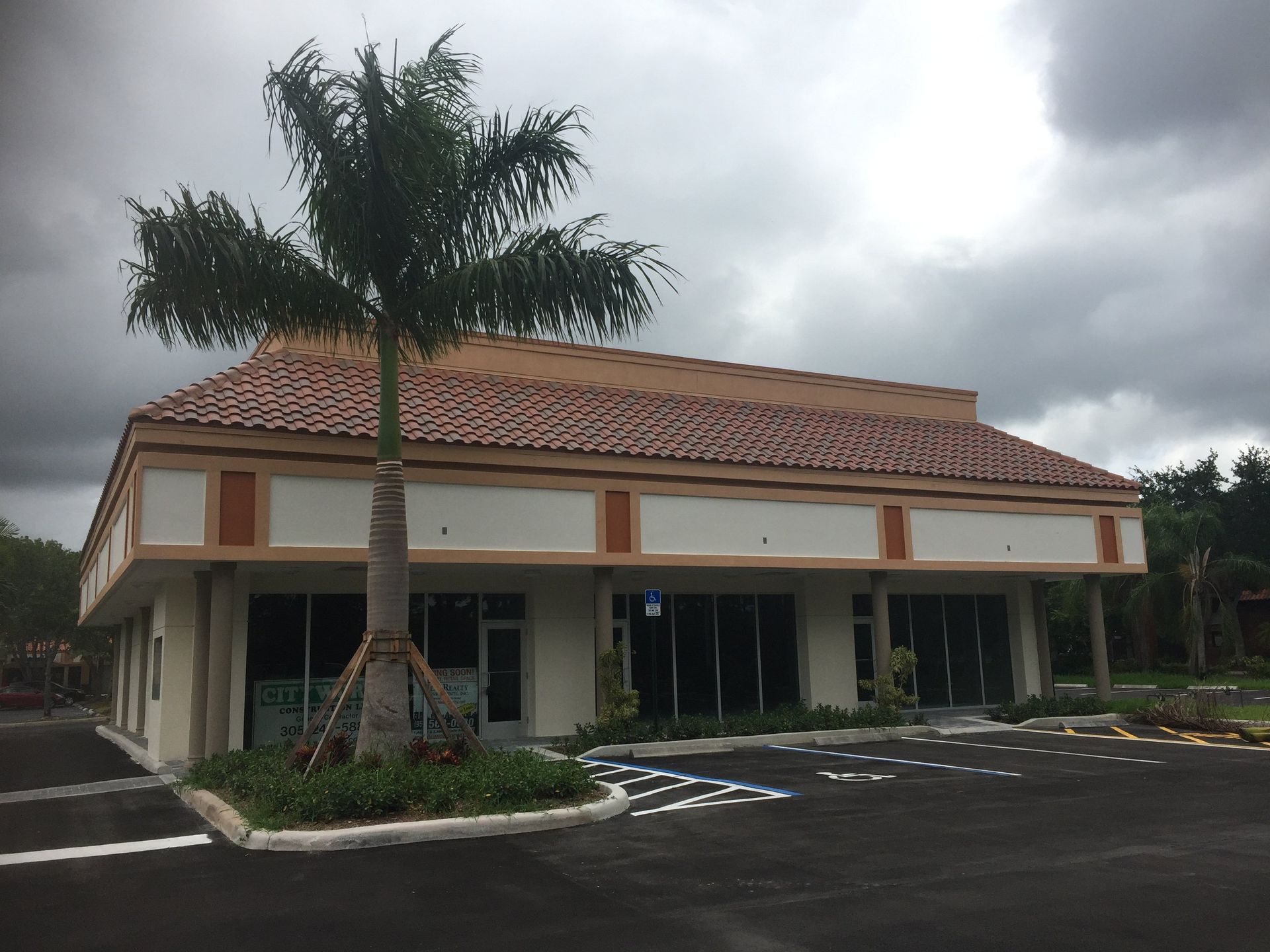 Exterior view of a commercial building with brown tile roof, cream-colored walls, and a palm tree.