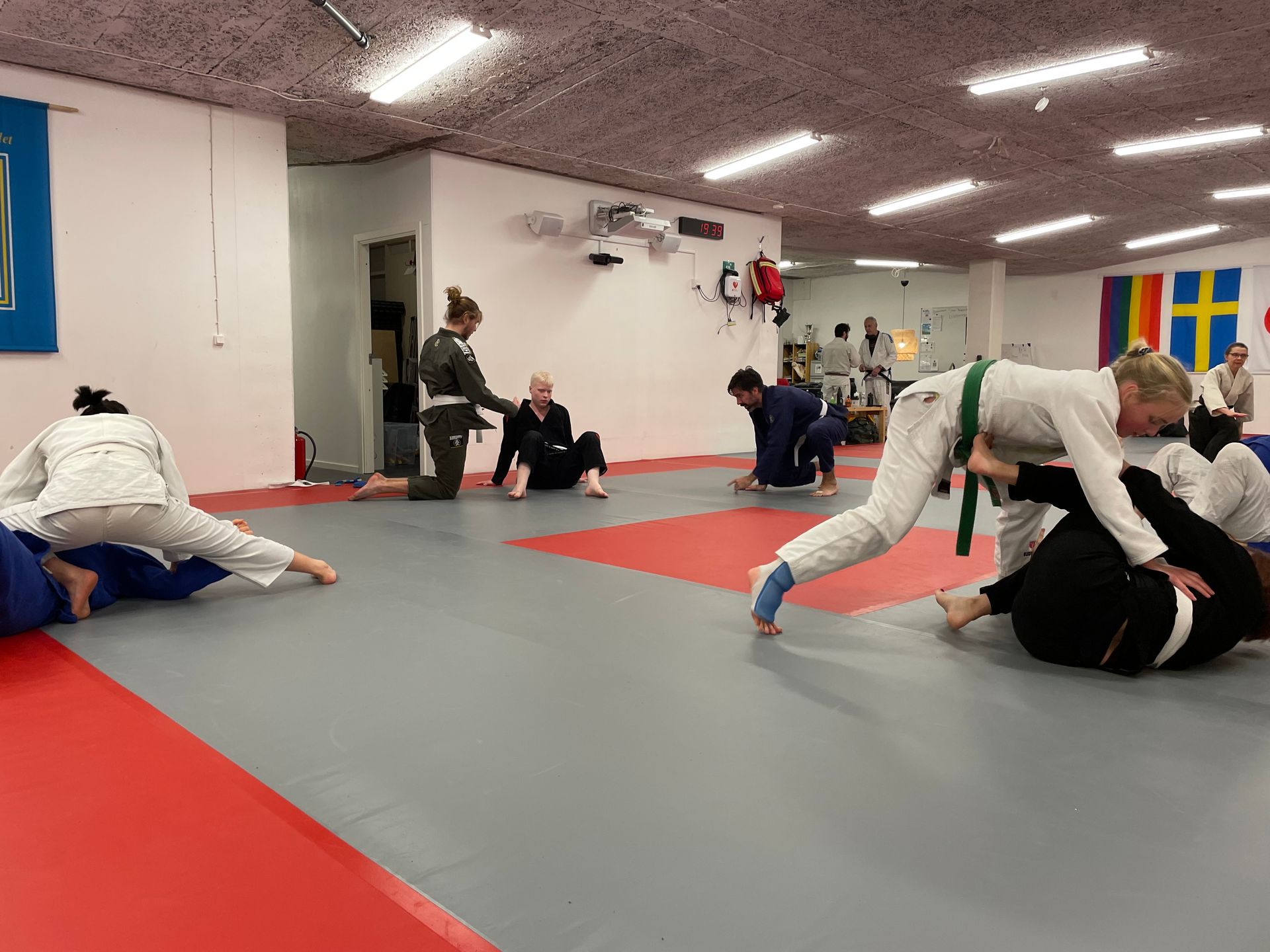 Människor i en kampsportklass som övar på mattor. Flera i vita och mörka gier