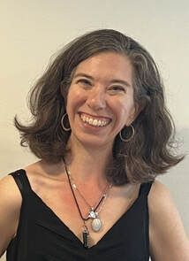A woman wearing a black tank top and a necklace is smiling.