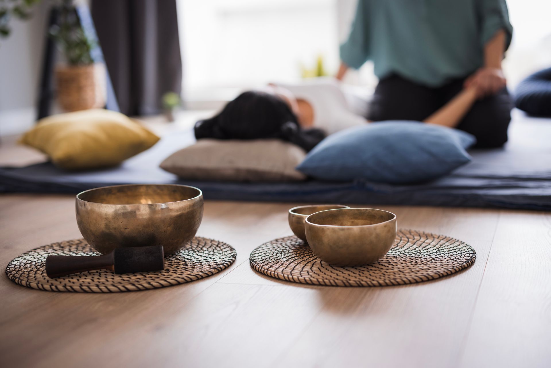 Sound bowls on mats in front of person lying down, with someone's hands on person.