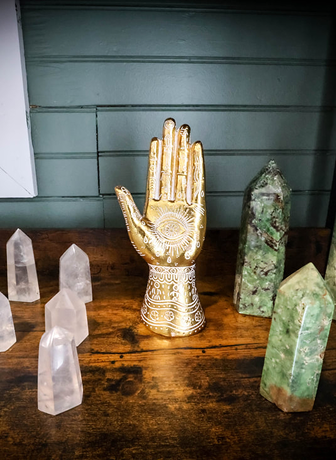 A gold hand statue is sitting on a wooden table next to crystals.