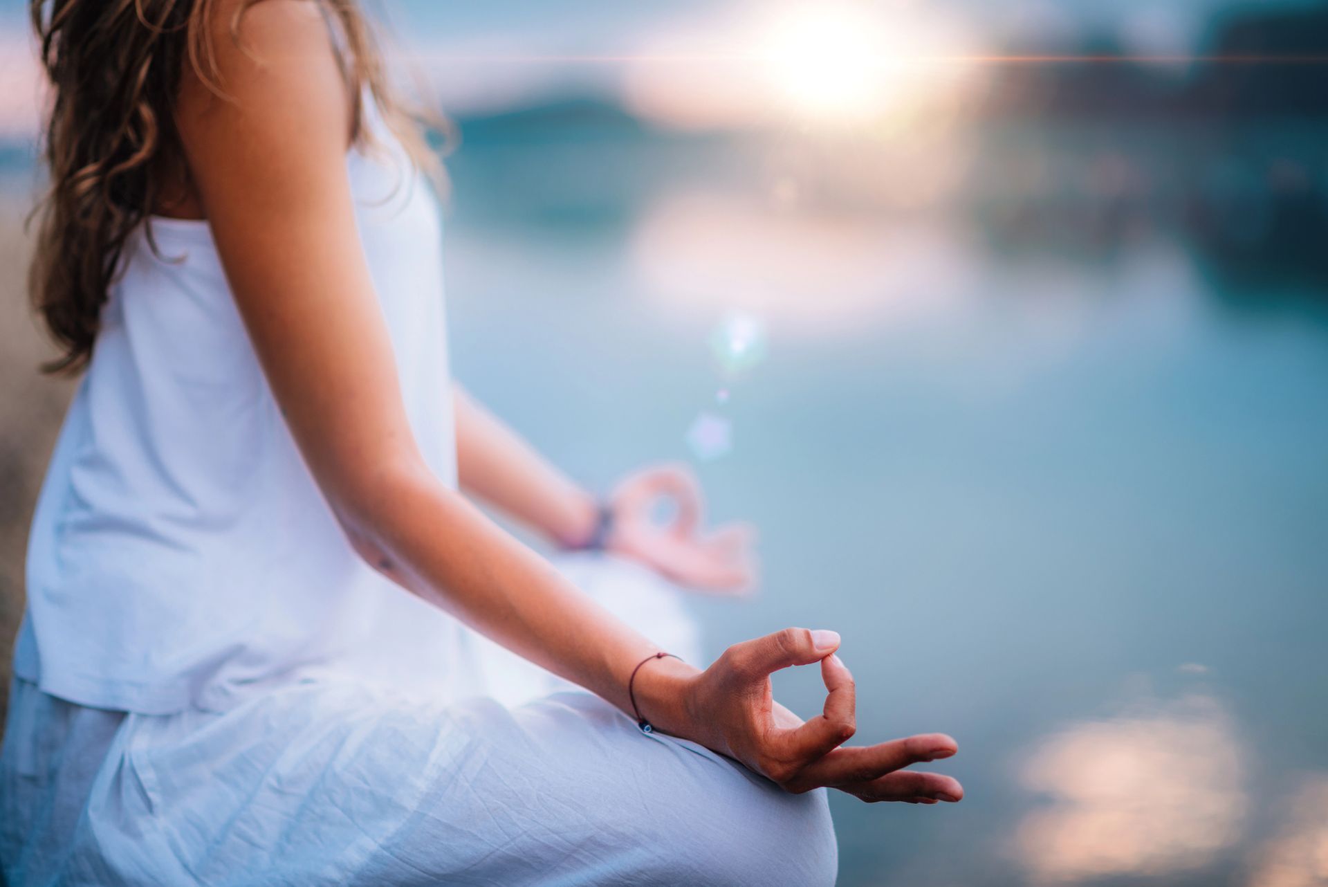 A woman in a white dress is sitting in a lotus position on the beach.